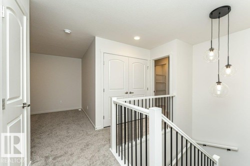 Upper landing featuring a contemporary three-light pendant, carpeted flooring, and a white staircase with black spindles - 6298 180 Avenue, Edmonton, AB - Indoor Photo Showing Other Room