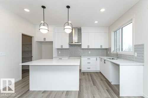 The kitchen features white cabinetry, a large island with a white countertop, and modern pendant lighting - 6298 180 Avenue, Edmonton, AB - Indoor Photo Showing Kitchen With Upgraded Kitchen