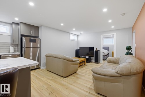 The open concept living area features light-colored flooring, recessed lighting, and a kitchen with stainless steel appliances, grey cabinetry, a light-colored countertop, and a white subway tile backsplash - 10612 79 Street, Edmonton, AB - Indoor