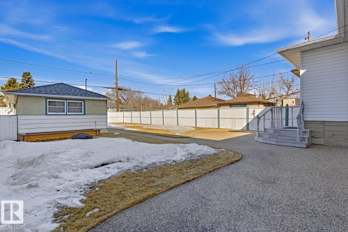 The property features a detached building with a dark roof and light-colored siding, a paved surface, and a white fence enclosing the yard - 10612 79 Street, Edmonton, AB - Outdoor
