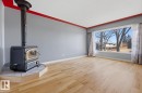 Living area featuring light wood flooring, a corner wood-burning stove with a tiled base, and a large window providing views of trees and other properties - 10612 79 Street, Edmonton, AB  - Indoor Photo Showing Other Room 