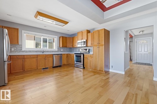 The kitchen features light wood cabinetry, stainless steel appliances, a light-colored backsplash, and hardwood floors - 10612 79 Street, Edmonton, AB - Indoor Photo Showing Kitchen