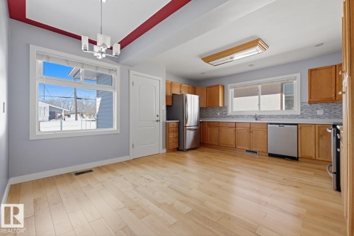 This inviting kitchen and dining area features light hardwood flooring, ample cabinetry, stainless steel appliances, and a tiled backsplash - 10612 79 Street, Edmonton, AB - Indoor Photo Showing Kitchen