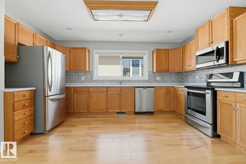 The kitchen features wood cabinetry, stainless steel appliances, a tile backsplash, and light-toned flooring - 10612 79 Street, Edmonton, AB - Indoor Photo Showing Kitchen