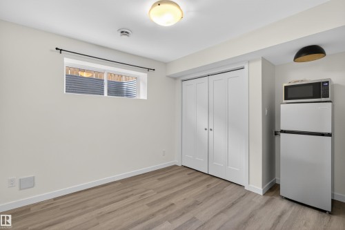 This room features durable plank flooring, a pair of bi-fold closet doors, a window with horizontal blinds, and a refrigerator with a microwave above - 42 Prescott Boulevard, Spruce Grove, AB - Indoor Photo Showing Other Room