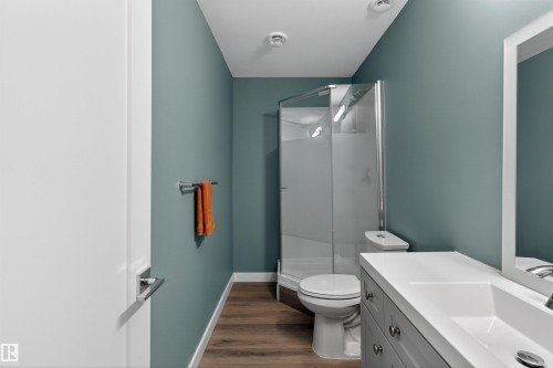 The bathroom features a corner shower, a vanity with a white countertop and integrated sink, and wood-style flooring - 42 Prescott Boulevard, Spruce Grove, AB - Indoor Photo Showing Bathroom