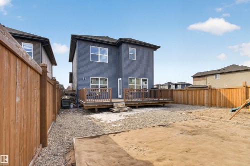 The property features a two-story exterior with siding, a wooden deck, and a fenced backyard with gravel and a sand area - 42 Prescott Boulevard, Spruce Grove, AB - Outdoor With Deck Patio Veranda With Exterior