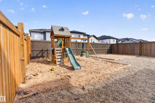 The fenced backyard features a play structure with a slide and swings, a large sand area, and a gravel section - 42 Prescott Boulevard, Spruce Grove, AB - Outdoor