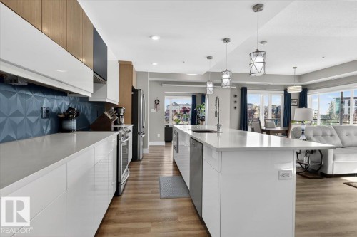 The kitchen features white cabinetry, a blue geometric tile backsplash, and stainless steel appliances - 214 528 Griesbach Parade Parade, Edmonton, AB - Indoor Photo Showing Kitchen With Upgraded Kitchen