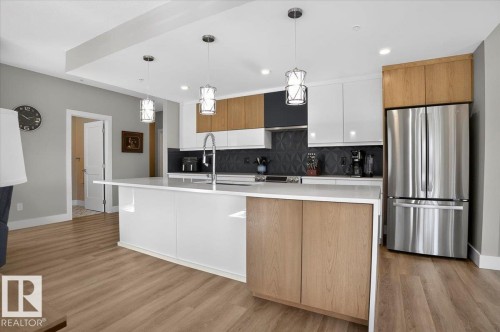 The property features a bright kitchen with light-toned flooring, a spacious island with a white countertop, stainless steel appliances, and sleek cabinetry in both light wood and white finishes - 214 528 Griesbach Parade Parade, Edmonton, AB - Indoor Photo Showing Kitchen With Stainless Steel Kitchen With Upgraded Kitchen