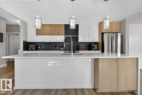 Modern kitchen featuring a large island with white countertops, stainless steel appliances, and sleek cabinetry in a mix of white and wood tones - 214 528 Griesbach Parade Parade, Edmonton, AB - Indoor Photo Showing Kitchen