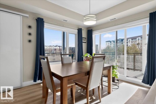 The property features an open dining area with light wood flooring, a modern pendant light fixture, and expansive windows - 214 528 Griesbach Parade Parade, Edmonton, AB - Indoor Photo Showing Dining Room