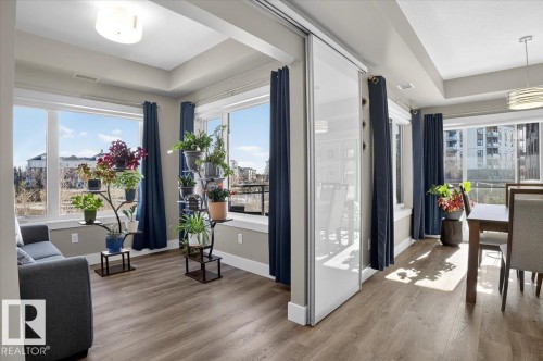 The open-concept living space features light wood-look flooring and large windows, providing abundant natural light - 214 528 Griesbach Parade Parade, Edmonton, AB - Indoor