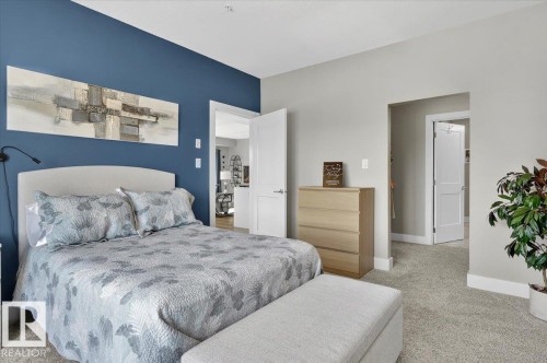 Bedroom with carpeted flooring, a feature wall painted in a deep blue hue, and white trim - 214 528 Griesbach Parade Parade, Edmonton, AB - Indoor Photo Showing Bedroom