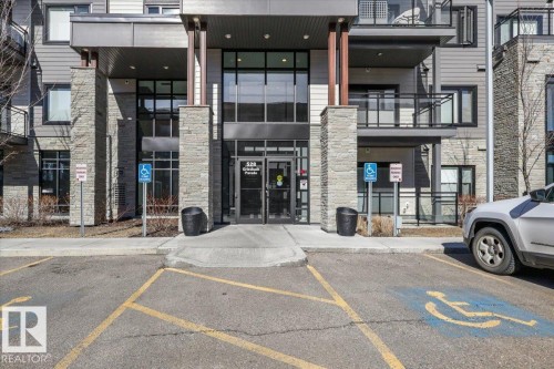The property features a modern exterior with stone and siding accents, a glass entrance, and balconies with glass railings - 214 528 Griesbach Parade Parade, Edmonton, AB - Outdoor With Balcony With Facade