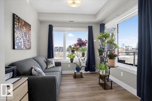 This room features large windows with dark blue curtains, providing ample natural light and views - 214 528 Griesbach Parade Parade, Edmonton, AB - Indoor Photo Showing Living Room
