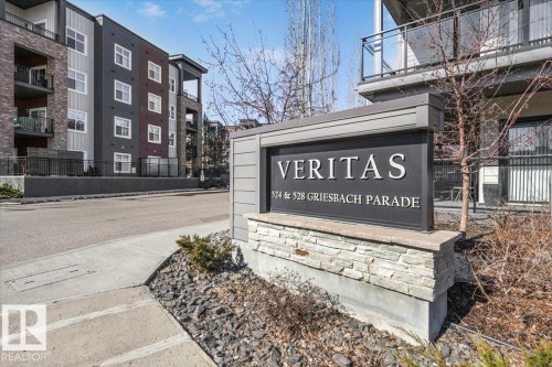 The property features a prominent entrance sign with a stone base, set against a backdrop of modern multi-story buildings with balconies - 214 528 Griesbach Parade Parade, Edmonton, AB - Outdoor With Balcony