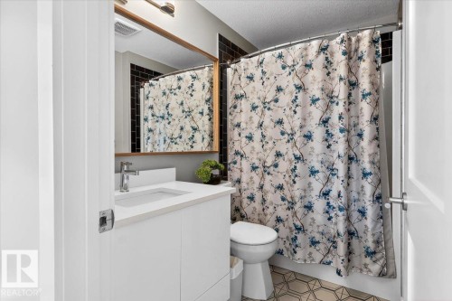 This bathroom features a contemporary vanity with a white countertop and an integrated sink, complemented by a large mirror with a wooden frame - 214 528 Griesbach Parade Parade, Edmonton, AB - Indoor Photo Showing Bathroom