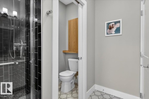 The property features a bathroom with a glass-enclosed shower, dark subway tile, and a toilet with an overhead wooden cabinet - 214 528 Griesbach Parade Parade, Edmonton, AB - Indoor Photo Showing Bathroom