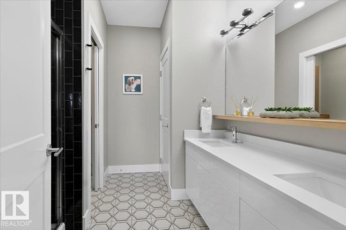 Bathroom featuring a floating double vanity with white countertops and integrated sinks, a large mirror, and patterned floor tiles - 214 528 Griesbach Parade Parade, Edmonton, AB - Indoor Photo Showing Bathroom
