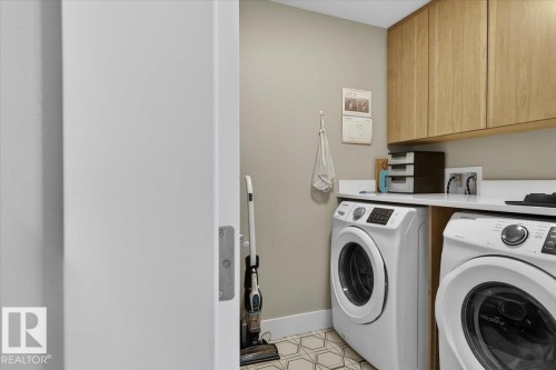 Laundry area featuring two front-loading machines, a white countertop, and light wood cabinetry - 214 528 Griesbach Parade Parade, Edmonton, AB - Indoor Photo Showing Laundry Room