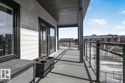 The property features a balcony with a glass railing, offering views of surrounding buildings and a clear sky - 214 528 Griesbach Parade Parade, Edmonton, AB - Outdoor With Balcony With Exterior