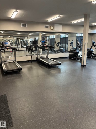 Fitness area featuring durable rubber flooring, mirrored walls, and various exercise equipment including treadmills and ellipticals - 214 528 Griesbach Parade Parade, Edmonton, AB - Indoor Photo Showing Gym Room