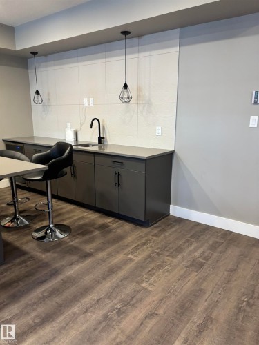Modern kitchen area featuring dark wood-look flooring, dark cabinetry, and a sink with a matte black faucet - 214 528 Griesbach Parade Parade, Edmonton, AB - Indoor
