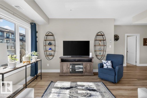 This inviting living area features light-colored walls, large windows providing natural light, and light wood-style flooring - 214 528 Griesbach Parade Parade, Edmonton, AB - Indoor Photo Showing Living Room