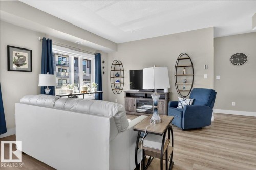The living area features light-toned flooring, a window with dark curtains, and light-colored walls - 214 528 Griesbach Parade Parade, Edmonton, AB - Indoor Photo Showing Living Room