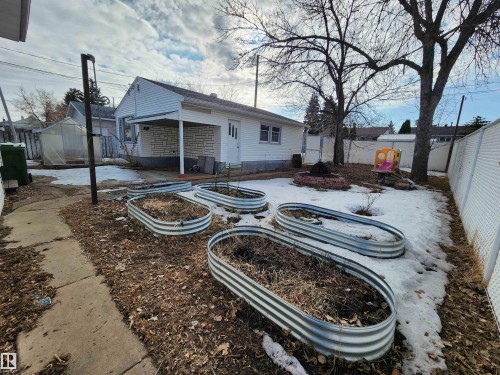 The property features a backyard with several raised garden beds, a fire pit, and mature trees - 10305 98 Avenue, Fort Saskatchewan, AB - Outdoor
