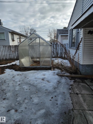 The property includes a greenhouse structure in the yard, which features a partial snow cover and a stone patio area - 10305 98 Avenue, Fort Saskatchewan, AB - Outdoor