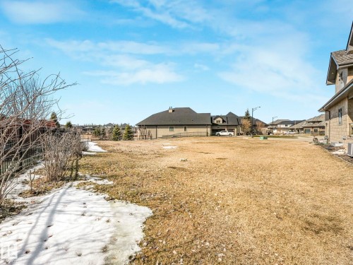 The property features an extensive yard with dry grass and patches of snow, bordered by a wooden fence and shrubs - 2794 Wheaton Drive, Edmonton, AB 