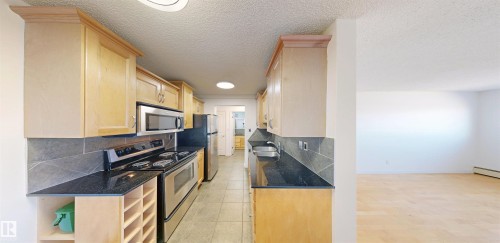 The kitchen features light wood cabinetry, stainless steel appliances, dark countertops, and a tiled backsplash - 303 8215 83 Avenue, Edmonton, AB - Indoor Photo Showing Kitchen With Stainless Steel Kitchen