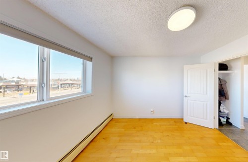 This room features warm-toned hardwood flooring and a large window, providing natural illumination - 303 8215 83 Avenue, Edmonton, AB - Indoor Photo Showing Other Room