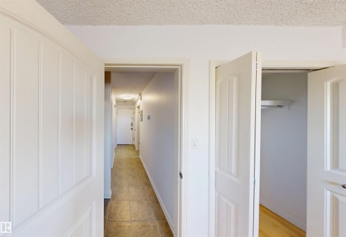 The property features a hallway with tiled flooring and white walls, leading to a closet with bifold doors and light wood flooring - 303 8215 83 Avenue, Edmonton, AB - Indoor Photo Showing Other Room