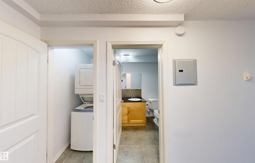 The property features a dedicated laundry area with a stacked washer and dryer, and a bathroom with a vanity and toilet - 303 8215 83 Avenue, Edmonton, AB - Indoor Photo Showing Laundry Room