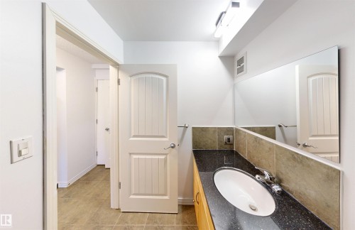 The bathroom features a vanity with a dark countertop, an undermount sink, and a large wall-mounted mirror - 303 8215 83 Avenue, Edmonton, AB - Indoor Photo Showing Bathroom