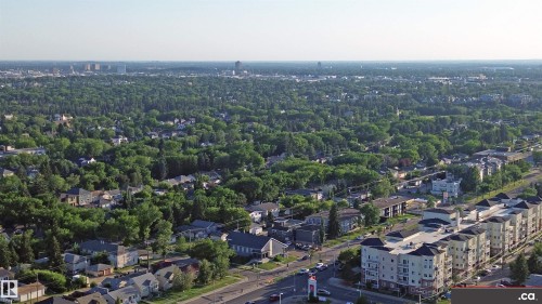 Expansive aerial view showcasing the surrounding area with a mix of residential properties, abundant green trees, and distant city skyline - 303 8215 83 Avenue, Edmonton, AB - Outdoor With View