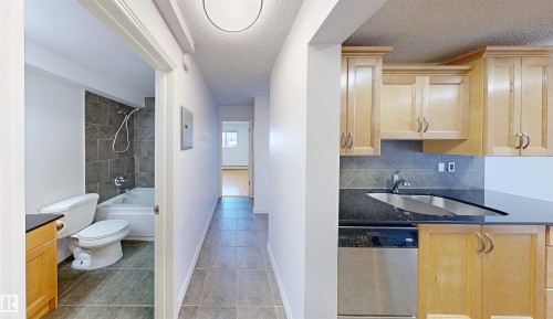 Kitchen featuring light wood cabinetry, black countertops, a stainless steel sink, and a stainless steel dishwasher - 303 8215 83 Avenue, Edmonton, AB - Indoor Photo Showing Bathroom