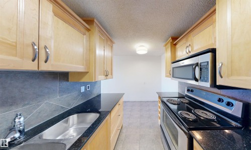 The kitchen features light-toned wooden cabinetry, dark countertops, and stainless steel appliances including a microwave and a range - 303 8215 83 Avenue, Edmonton, AB - Indoor Photo Showing Kitchen