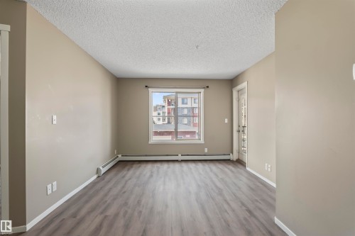 The living area features a window providing natural light, a textured ceiling, and wood-look flooring - 214 5816 Mullen Place, Edmonton, AB - Indoor Photo Showing Other Room