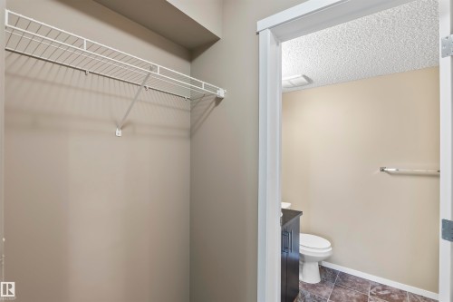 This property features a storage closet with a wire shelf, and a bathroom with a toilet, vanity, and tiled floors - 214 5816 Mullen Place, Edmonton, AB - Indoor