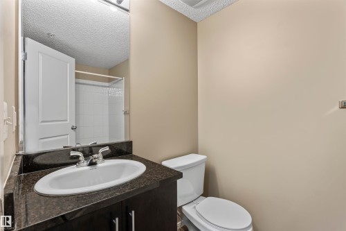 Bathroom featuring a dark vanity with an oval sink, a dark countertop, and a white toilet - 214 5816 Mullen Place, Edmonton, AB - Indoor Photo Showing Bathroom