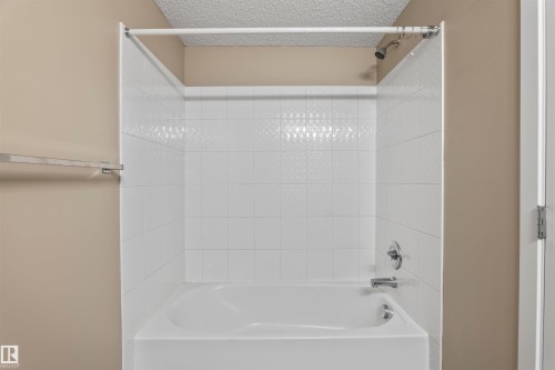 Bathroom featuring a bathtub with a shower, white tiled walls, and chrome fixtures - 214 5816 Mullen Place, Edmonton, AB - Indoor Photo Showing Bathroom