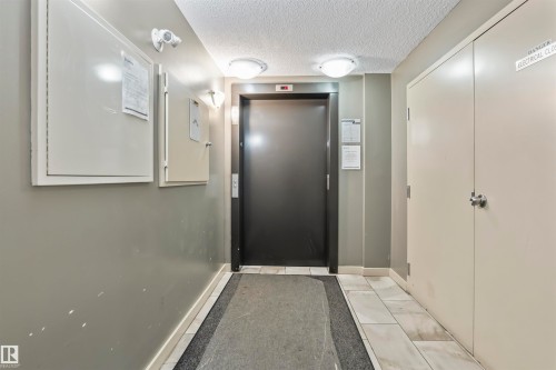 The property offers convenient access to an elevator and features a tiled floor, ceiling lighting, and wall-mounted light fixtures - 214 5816 Mullen Place, Edmonton, AB - Indoor Photo Showing Other Room