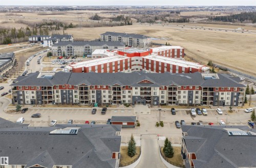 Aerial view of the property and surrounding buildings, featuring multi-story structures with balconies, ample parking, and an extensive surrounding landscape - 214 5816 Mullen Place, Edmonton, AB - Outdoor With View