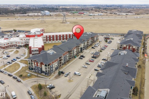 Aerial view of the property and surrounding area, featuring a large parking area and multiple buildings - 214 5816 Mullen Place, Edmonton, AB - Outdoor With View
