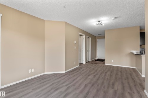 The property features an open living area with neutral-toned walls and grey plank flooring - 214 5816 Mullen Place, Edmonton, AB - Indoor Photo Showing Other Room