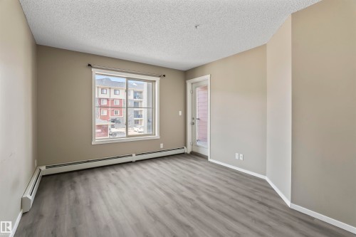 The property features an interior space with light gray walls, gray wood-look flooring, and a white ceiling - 214 5816 Mullen Place, Edmonton, AB - Indoor Photo Showing Other Room